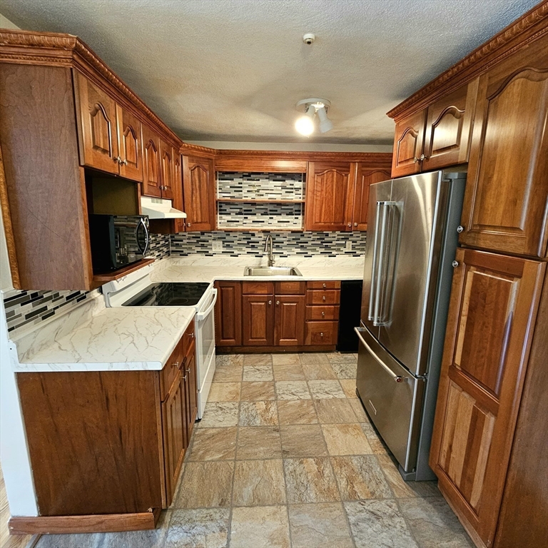 a kitchen with stainless steel appliances granite countertop a refrigerator a sink a stove top oven and cabinets