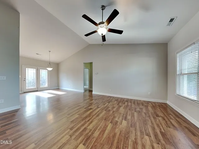 an empty room with wooden floor chandelier and windows