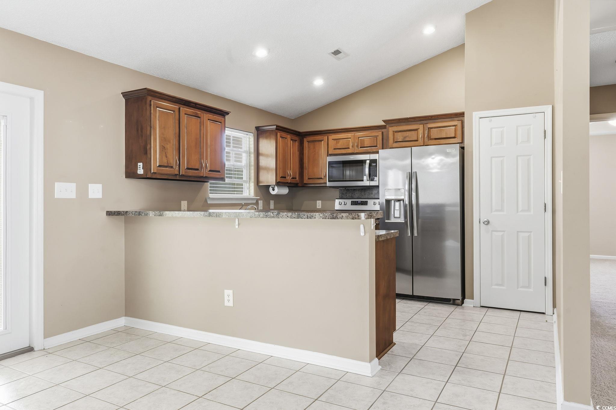 1007 Green Fir Loop Conway, SC 29527 - Photo 11 of 38 Kitchen featuring stainless steel appliances, a peninsula, vaulted ceiling, light tile patterned floors, and brown cabinets