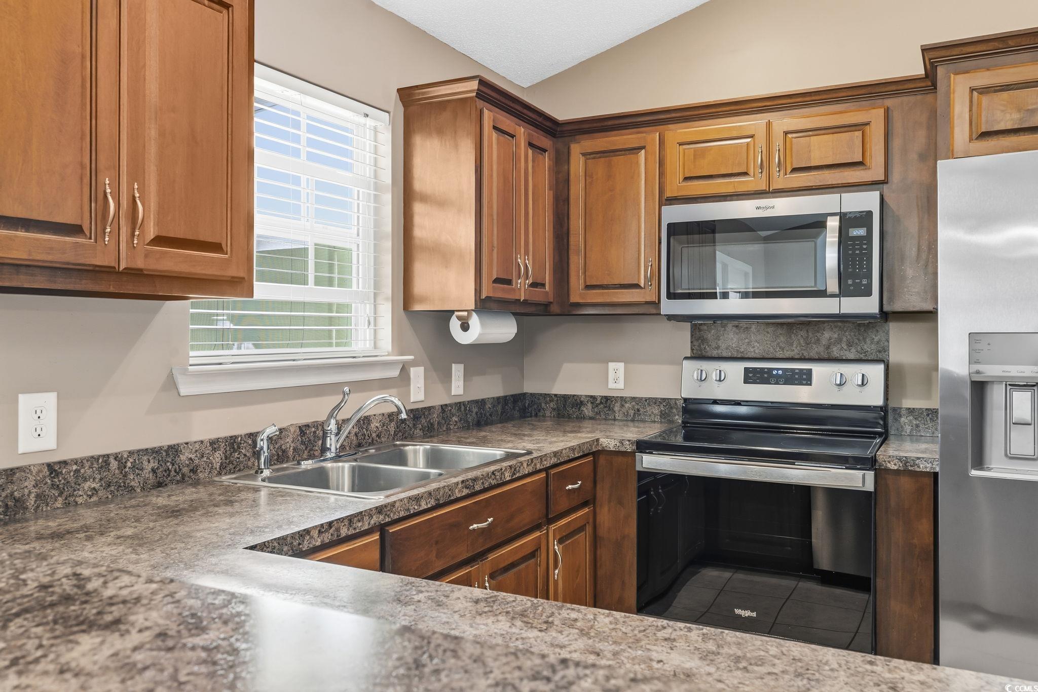 1007 Green Fir Loop Conway, SC 29527 - Photo 15 of 38 Kitchen featuring stainless steel appliances, dark countertops, brown cabinetry, lofted ceiling, and tile patterned floors