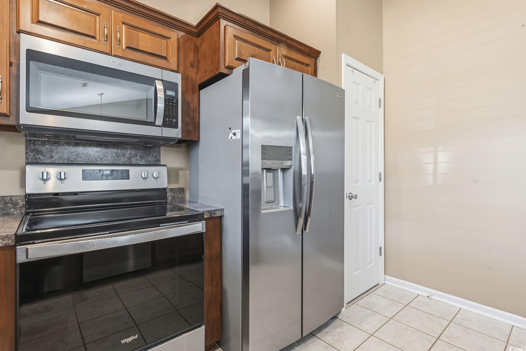 1007 Green Fir Loop Conway, SC 29527 - Photo 17 of 38 Kitchen with stainless steel appliances, dark countertops, light tile patterned floors, and brown cabinets