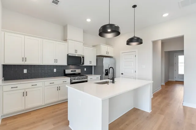 a kitchen with stainless steel appliances a stove a sink a dining table and chairs with wooden floor