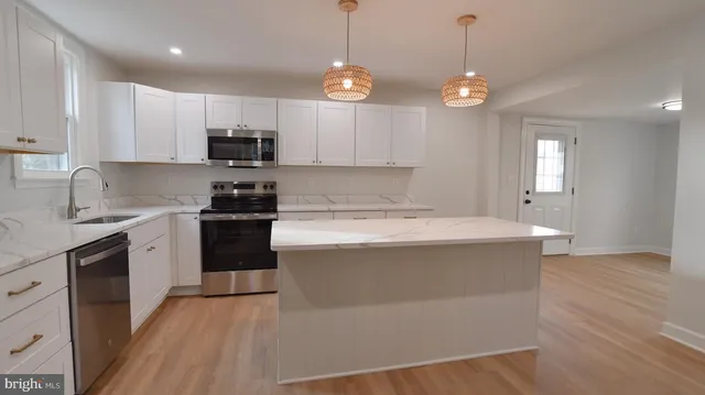 a kitchen with stainless steel appliances granite countertop a sink a stove a refrigerator and white cabinets with wooden floor