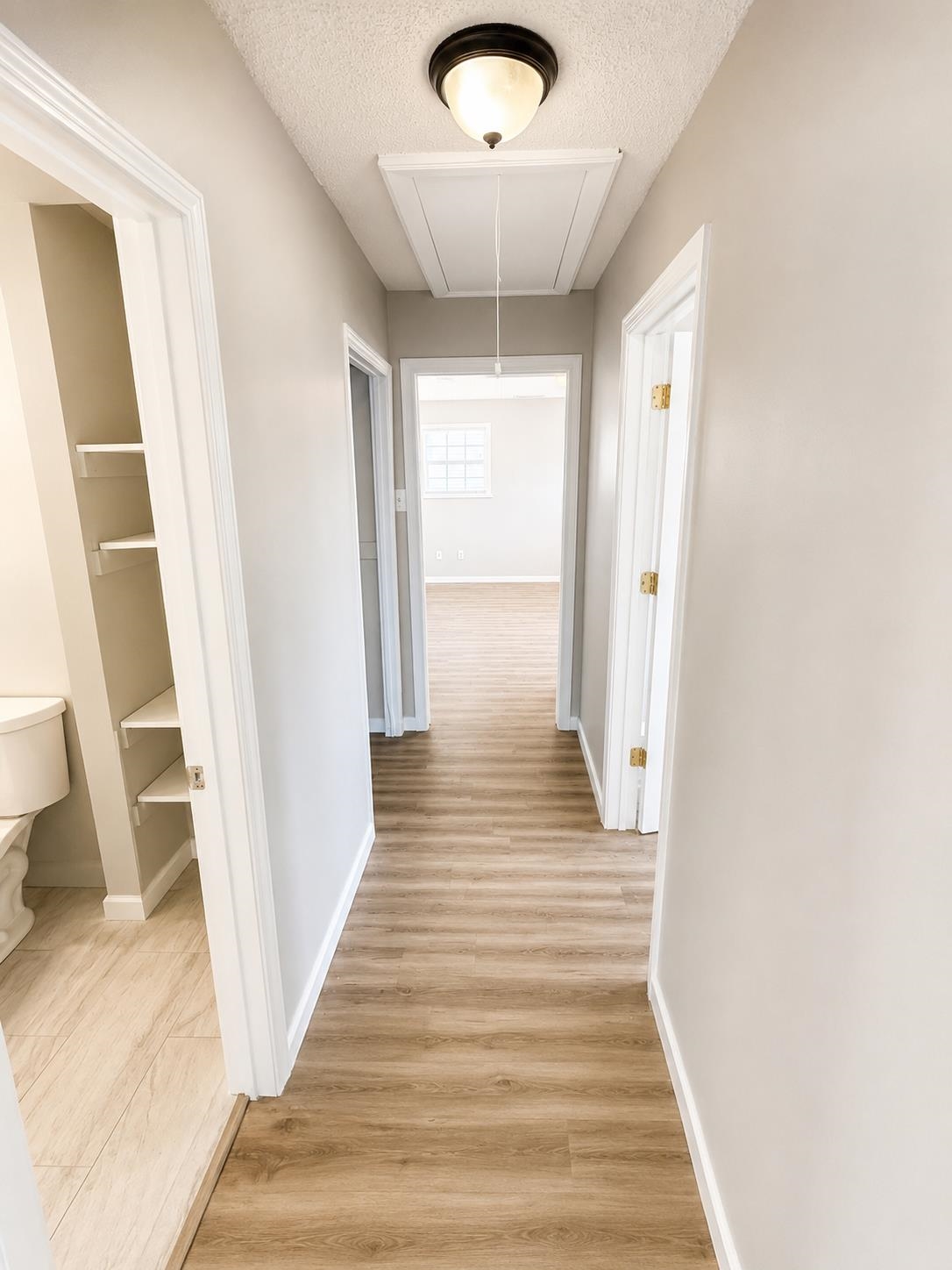 Hallway featuring wood-finish flooring, light neutral wall paint, and overhead flush-mount lighting