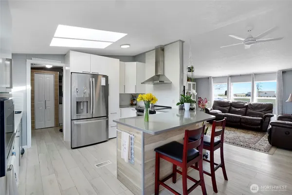 a kitchen with stainless steel appliances kitchen island granite countertop a refrigerator a stove a dining table and chairs with wooden floor