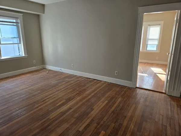 a view of an empty room with wooden floor and a window