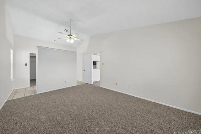 an empty room with chandelier fan and windows