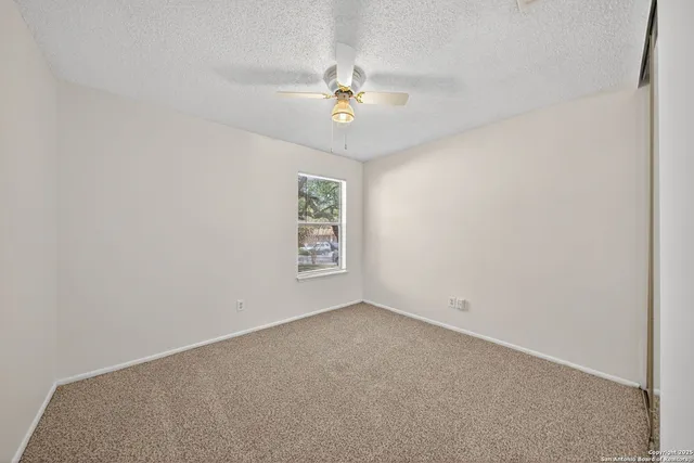 an empty room with a chandelier fan and windows