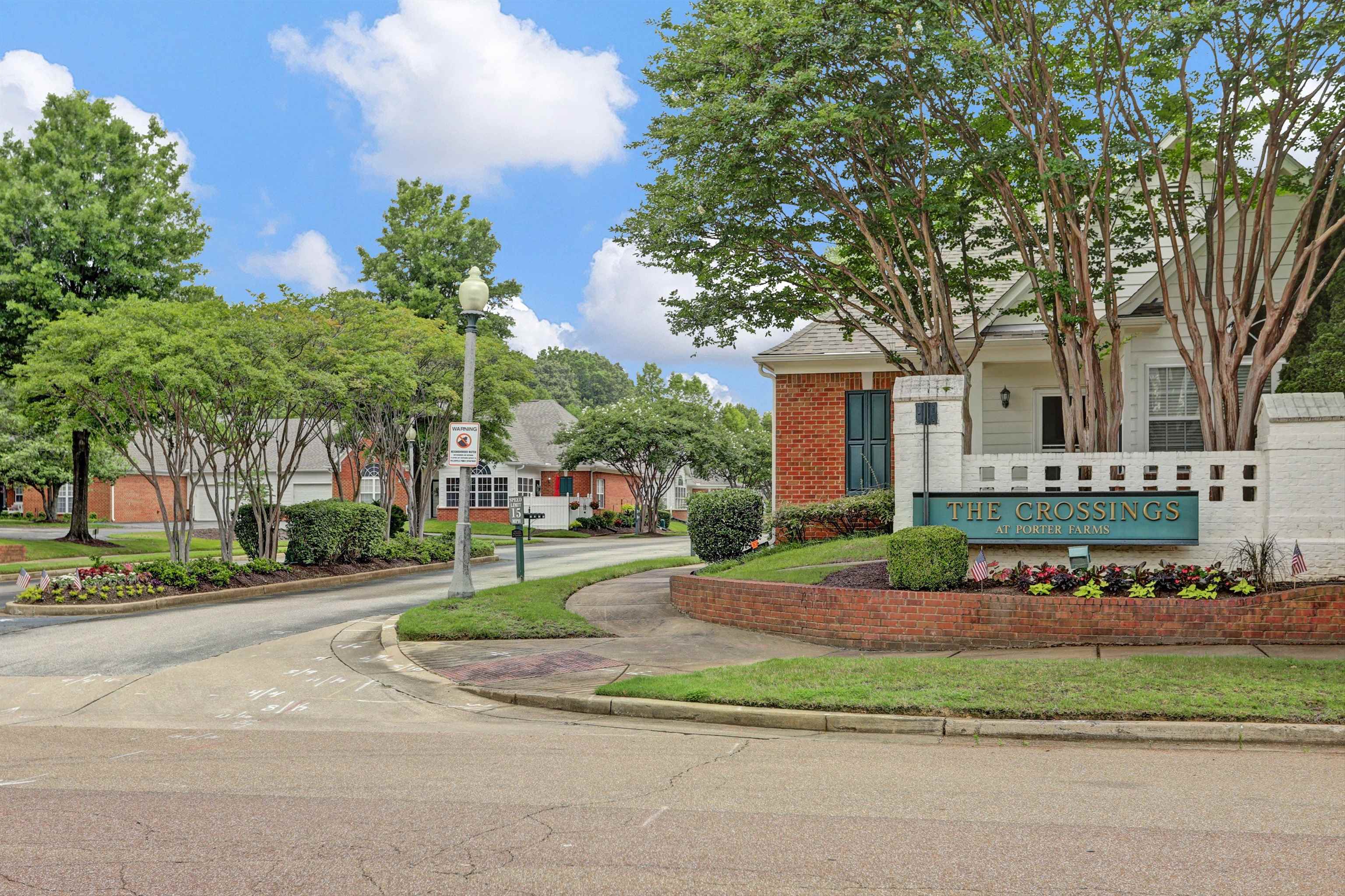 34 Peyton Ridge Drive, Unit 21 Collierville, TN 38017 - Photo 36 of 37 Entryway featuring a brick-faced sign with "The Crossings" inscription, surrounded by manicured landscaping, mature trees, and a brick retaining wall