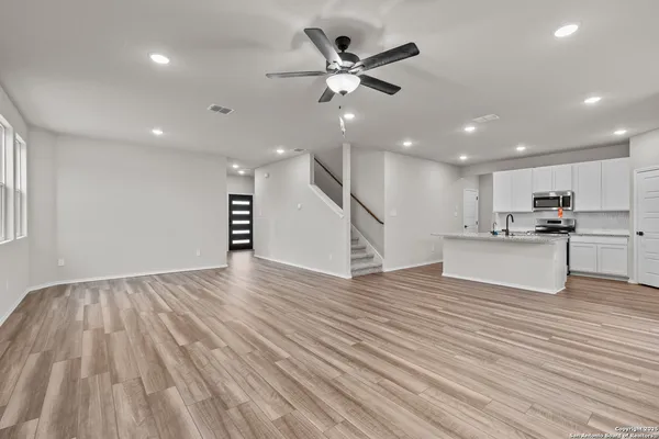 a view of an empty room with wooden floor and a ceiling fan
