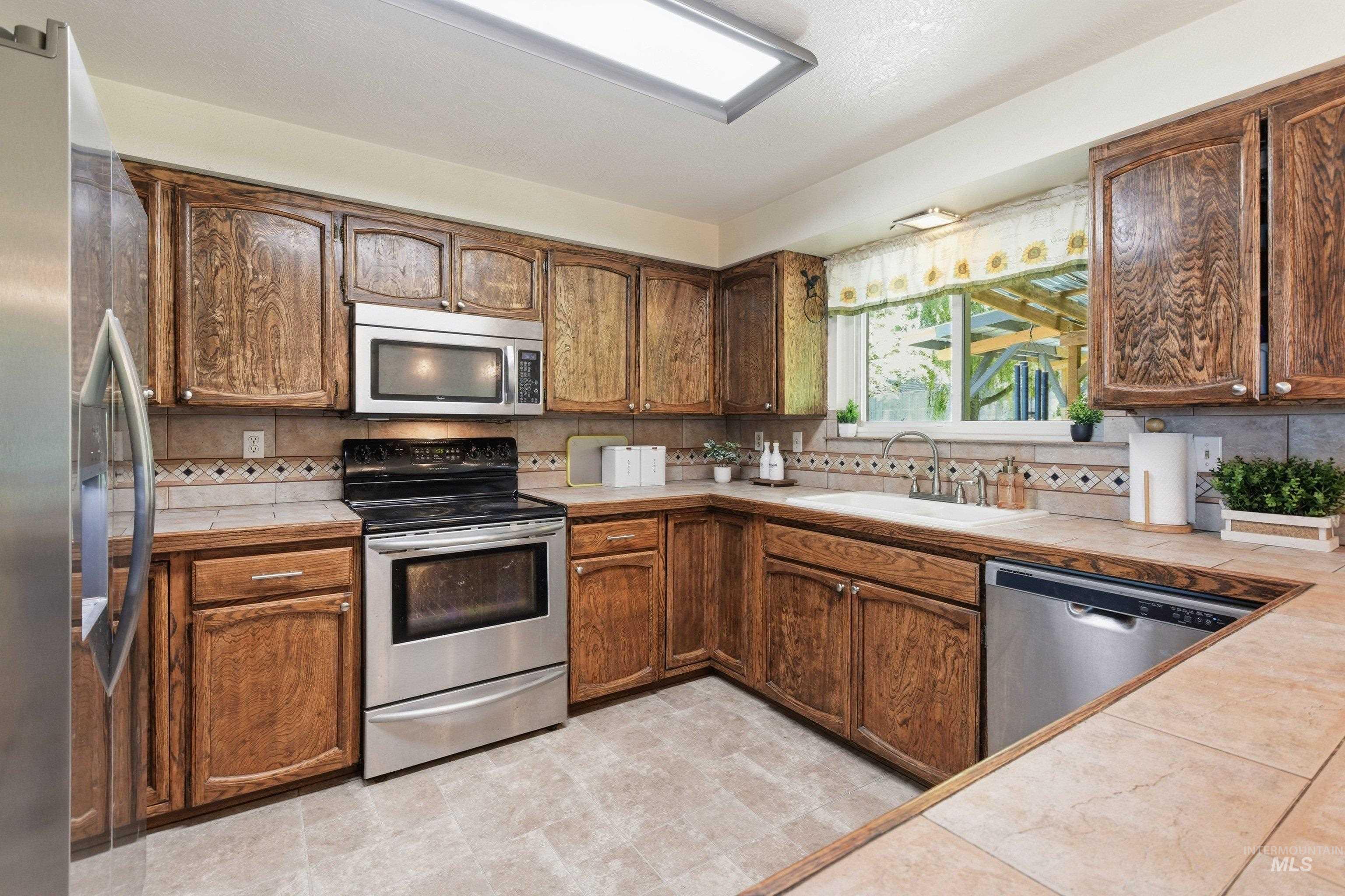 15095 David Street Caldwell, ID 83607 - Photo 15 of 39 Kitchen featuring wood cabinetry, stainless steel appliances, tile flooring, and tile countertops with a decorative tile backsplash