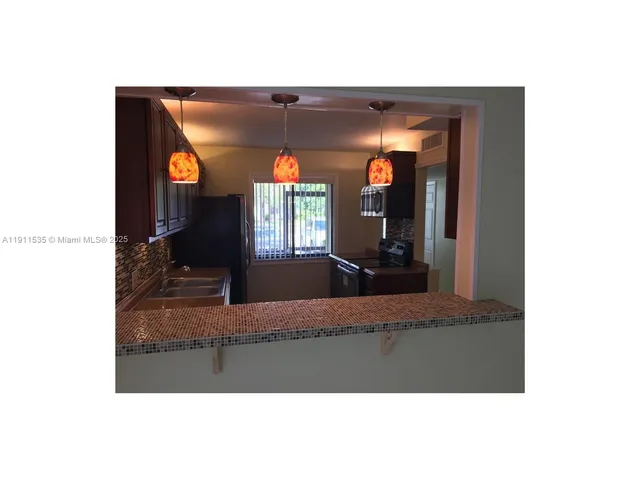 a view of a living room with chandelier fan and kitchen view
