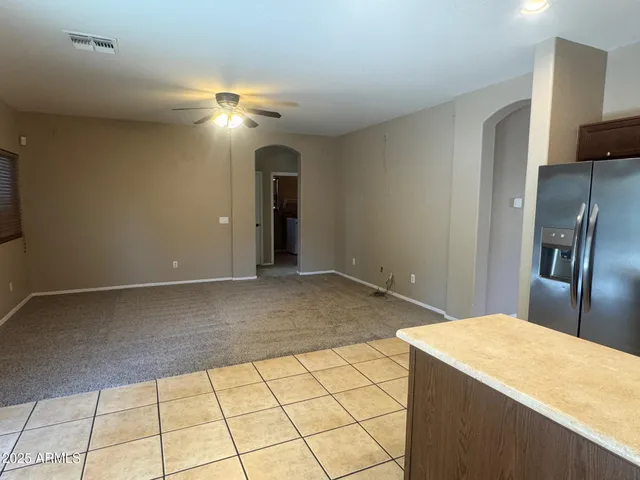 a room with a chandelier fan and kitchen view
