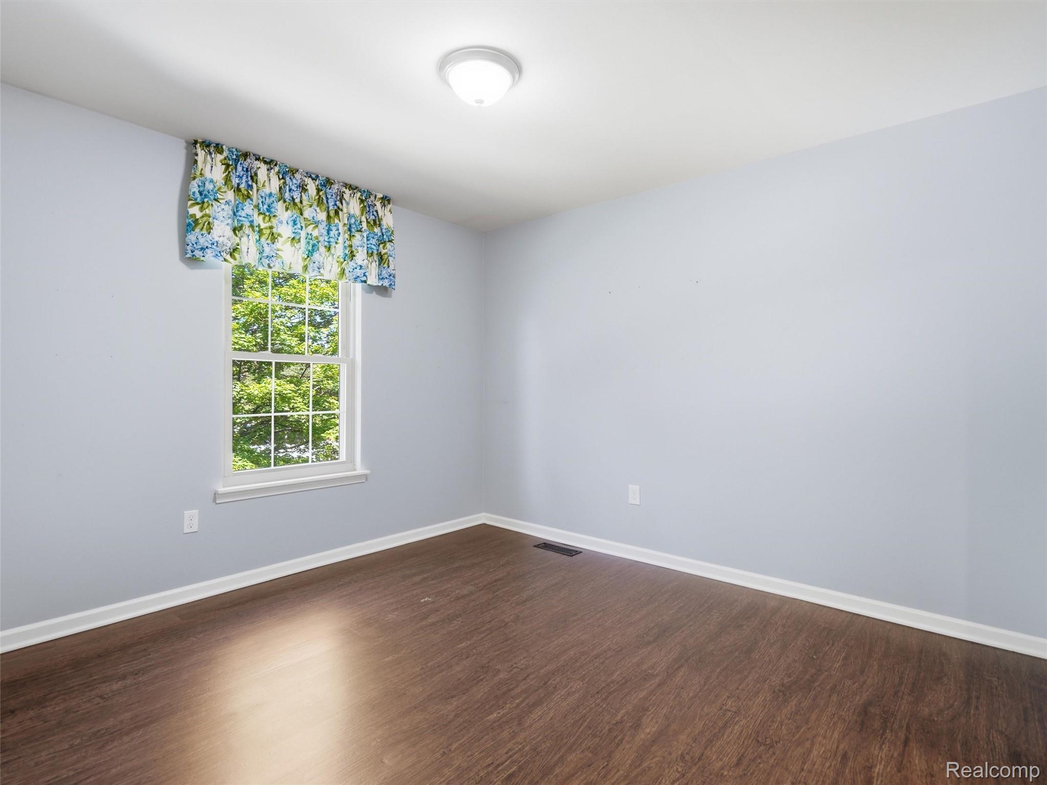 29636 Middlebelt Road, Unit 2602 Farmington, MI 48334 - Photo 11 of 34 Bright interior space featuring a window with natural light, light blue wall paint, wood-finish flooring, white baseboards, and a ceiling-mounted light fixture