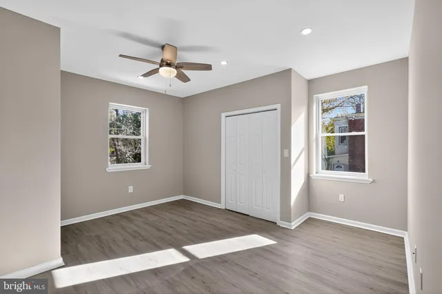 an empty room with wooden floor ceiling fan and windows