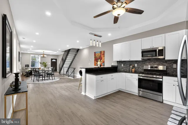 a kitchen with stainless steel appliances kitchen island granite countertop a stove top oven a sink a dining table and chairs with wooden floor