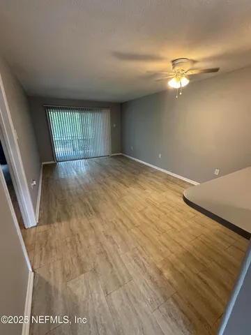 a view of an empty room with wooden floor and fan