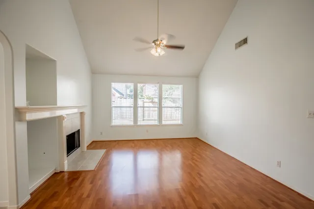 an empty room with wooden floor a ceiling fan and windows