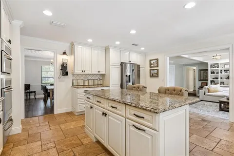a kitchen with stainless steel appliances granite countertop a table chairs and a living room view