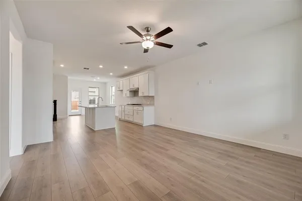 a view of an empty room with wooden floor and a kitchen