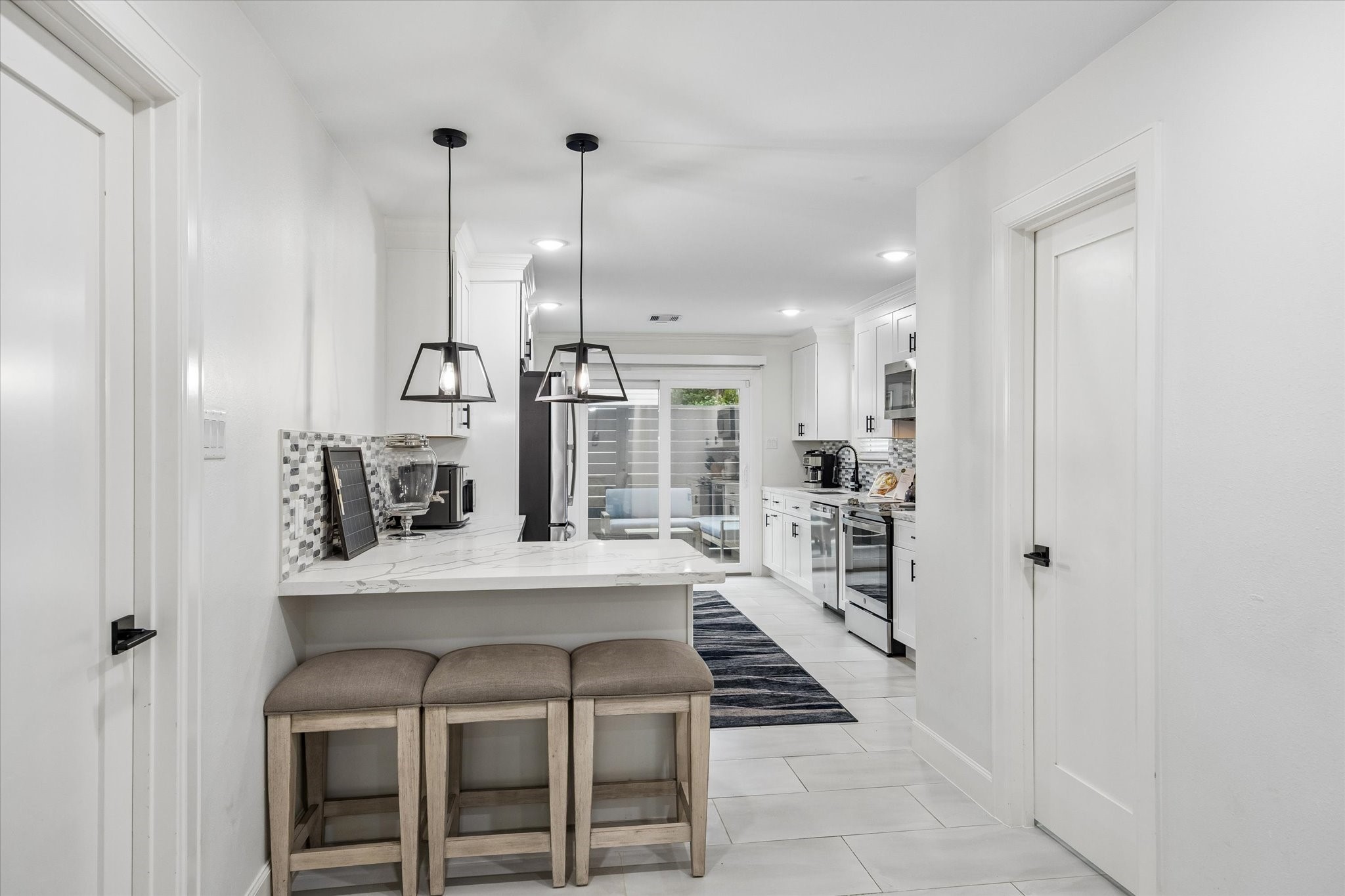 1420 Indiana Street Houston, TX 77006 - Photo 15 of 31 Bright, modern kitchen featuring white cabinetry, sleek stainless steel appliances, and a cozy breakfast bar with pendant lighting. The open layout connects to a living area with sliding glass doors, enhancing natural light.
