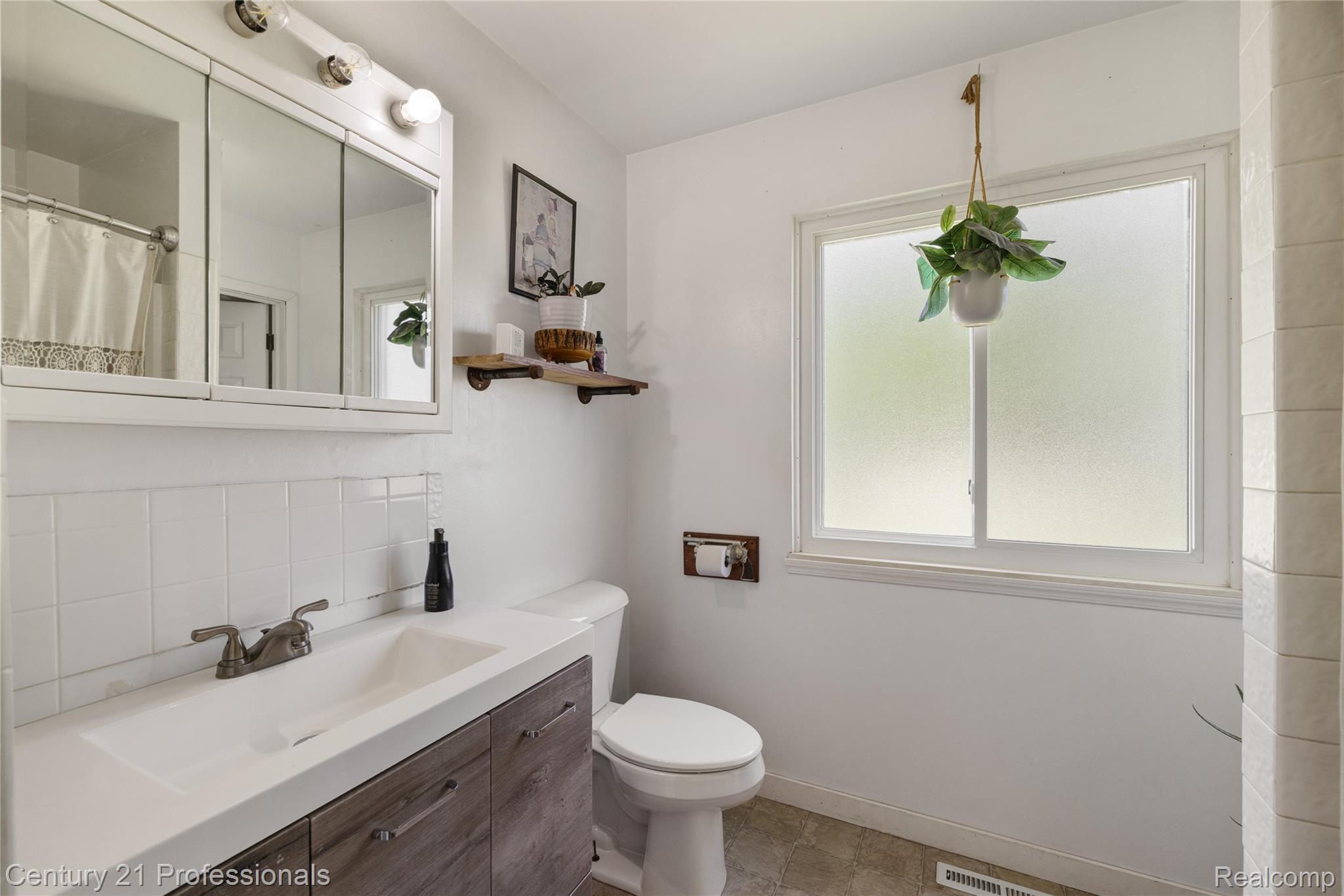 15037 Hogan Road Linden, MI 48451 - Photo 19 of 38 Bathroom featuring a wood-finish vanity with an integrated sink, a medicine cabinet, subway tile backsplash, a toilet, and a frosted window