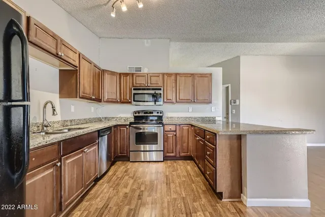 a kitchen with stainless steel appliances granite countertop a stove top oven a sink dishwasher a refrigerator and cabinets with wooden floor