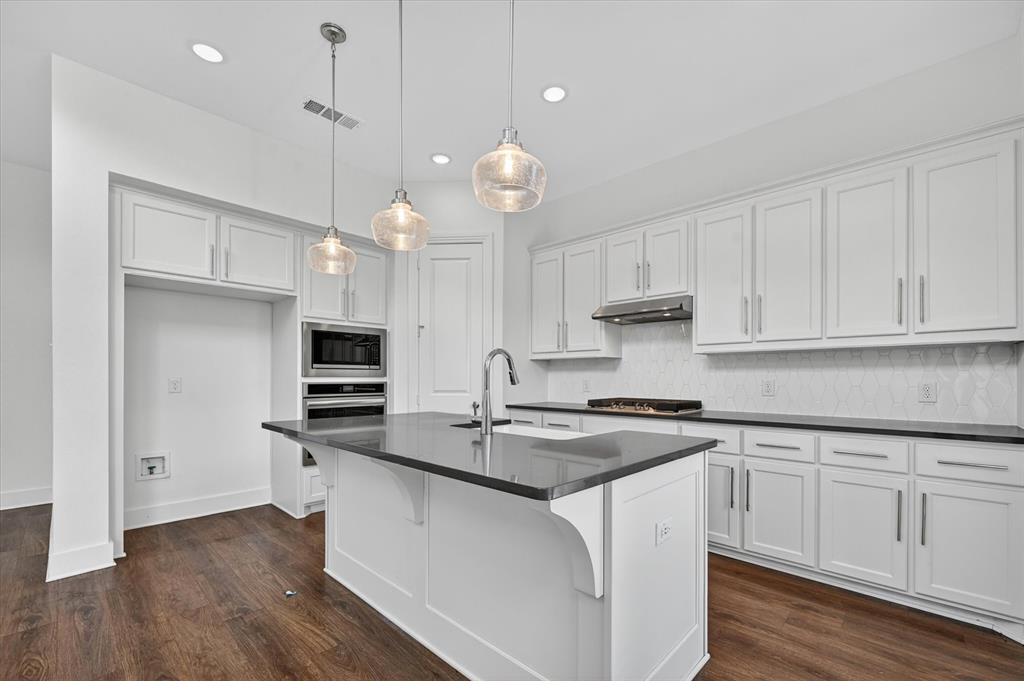 1153 Queensdown Way Forney, TX 75126 - Photo 8 of 26 Kitchen featuring a central island with a sink, pendant lighting, built-in microwave and oven, white shaker-style cabinetry, and dark countertops