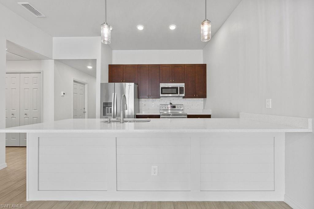 3429 Southwest 8th Place Cape Coral, FL 33914 - Photo 8 of 19 a large white kitchen with kitchen island granite countertop a sink a refrigerator and white cabinets