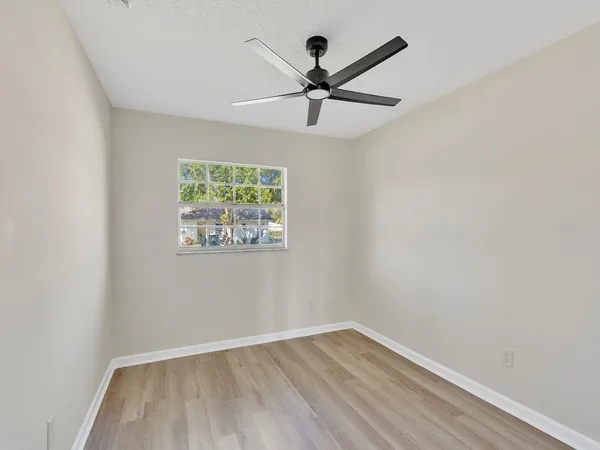 an empty room with wooden floor fan and windows