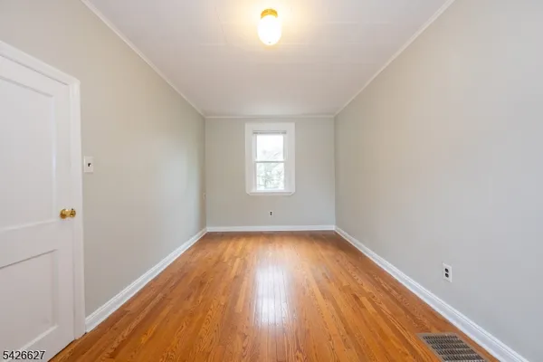 a view of an empty room with wooden floor and window