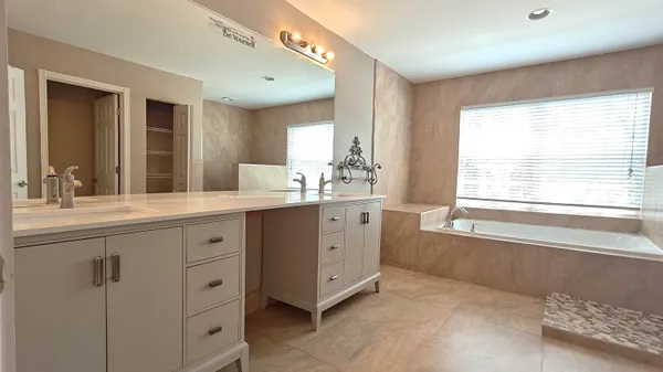 a bathroom with a double vanity sink a large mirror and a bathtub next to a window