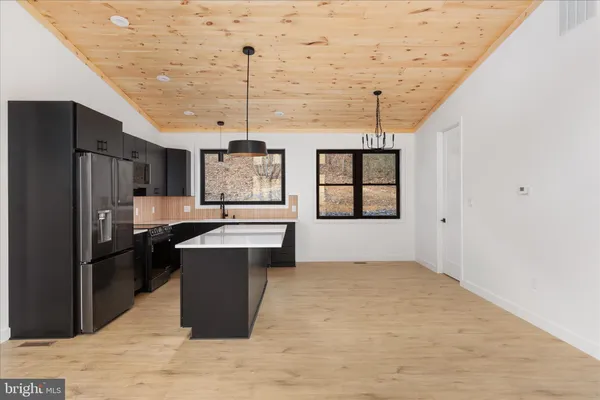 a kitchen with stainless steel appliances kitchen island granite countertop a refrigerator a sink dishwasher and white cabinets next to a window