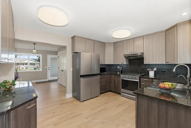 a kitchen with granite countertop a stove a sink dishwasher a refrigerator and a stove with wooden floor