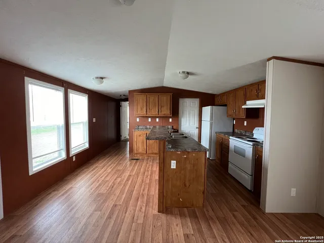 a kitchen with granite countertop a refrigerator a stove top oven a sink dishwasher and wooden floor