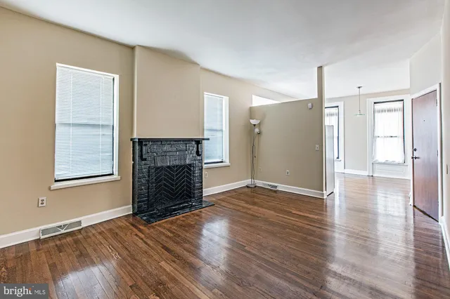 an empty room with wooden floor fireplace and windows