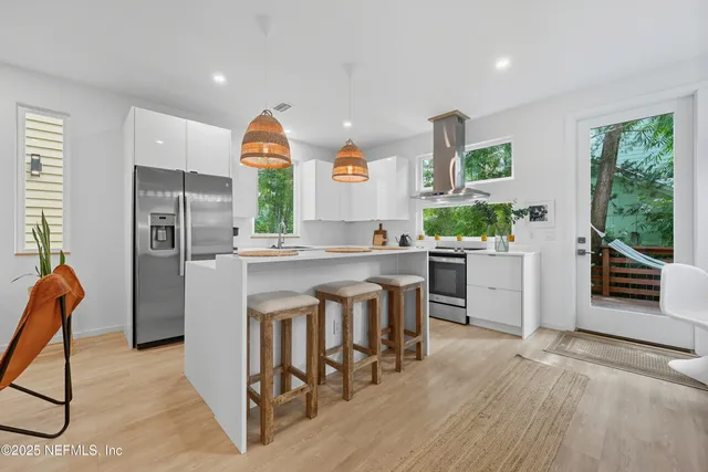 a kitchen with stainless steel appliances granite countertop a refrigerator a stove a sink a dining table and chairs with wooden floor