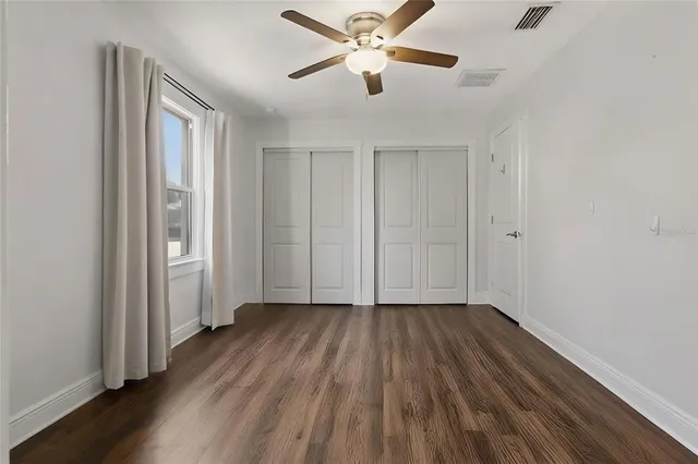 a view of an empty room with wooden floor and a ceiling fan