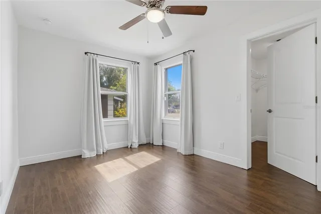 an empty room with wooden floor chandelier fan and windows