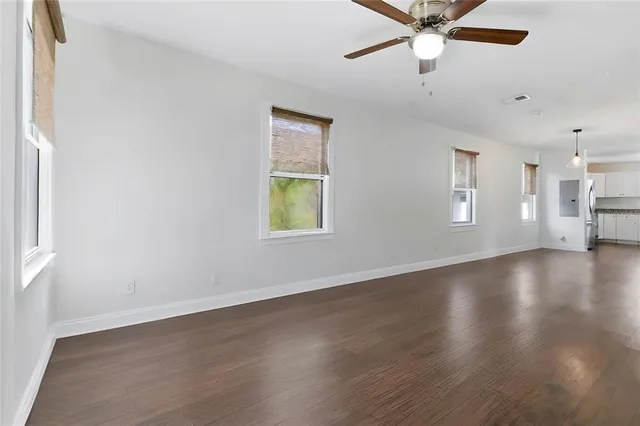 an empty room with wooden floor fan and windows