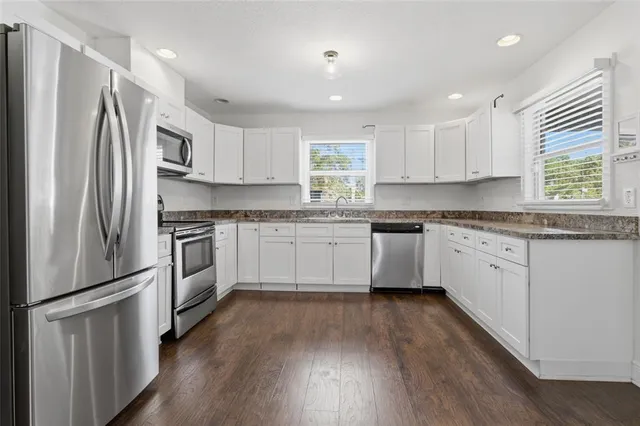 a kitchen with white cabinets stainless steel appliances a sink and a window