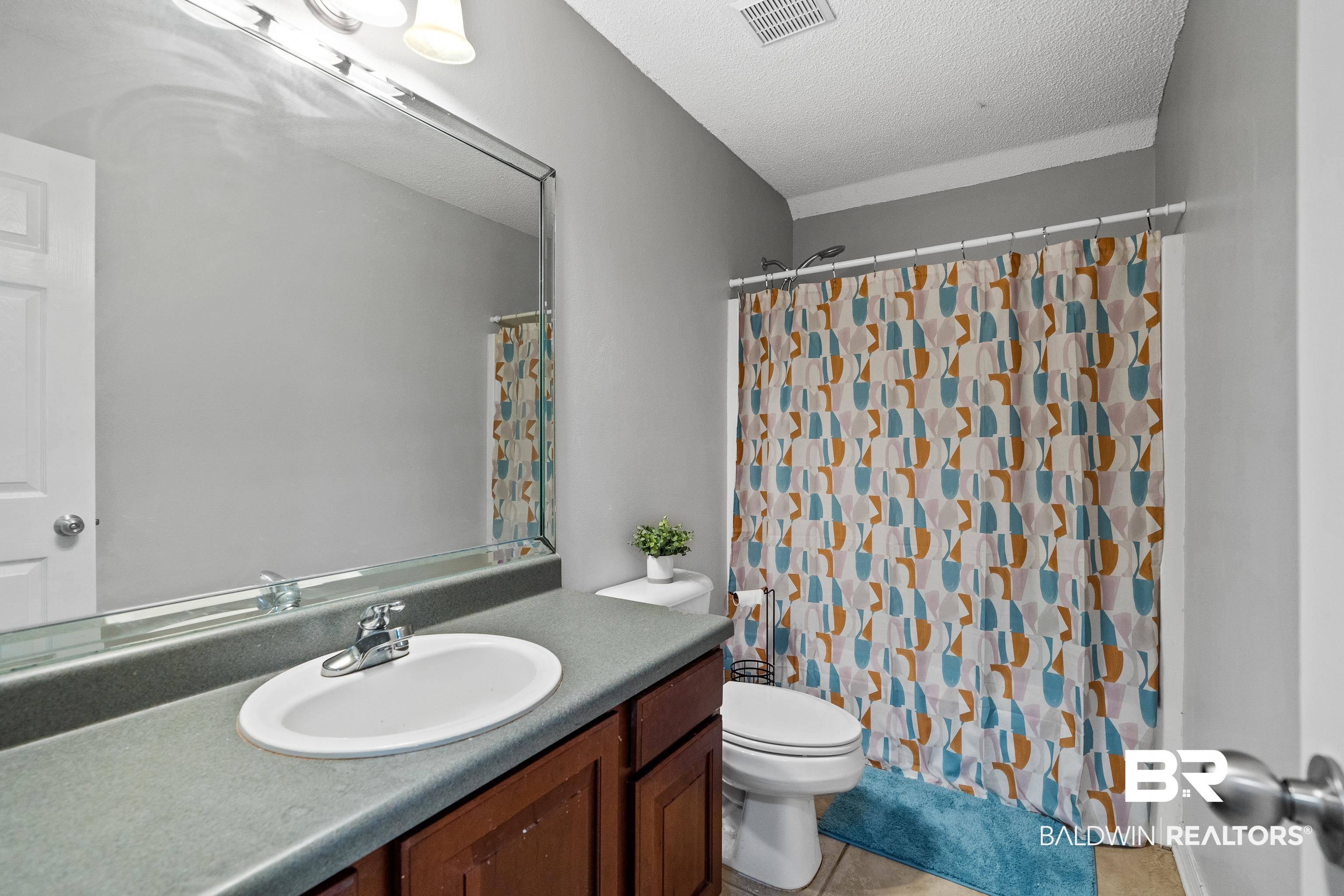 9552 Collier Loop Daphne, AL 36526 - Photo 21 of 28 Full bath with vanity, a textured ceiling, toilet, tile patterned floors, and a shower with curtain