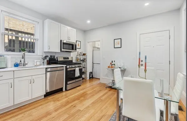 a kitchen with stainless steel appliances a stove top oven a sink a refrigerator and white cabinets with wooden floor