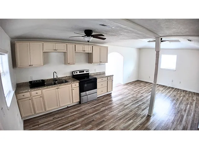 a kitchen with stainless steel appliances granite countertop a stove a sink and white cabinets with wooden floor