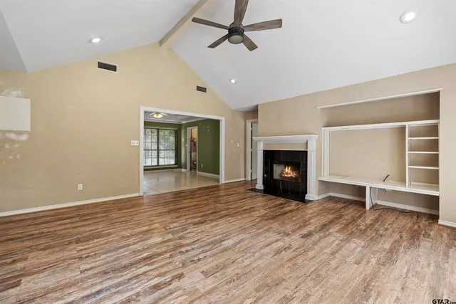 an empty room with wooden floor fireplace and windows