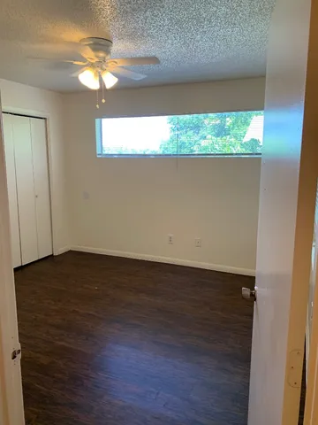 an empty room with wooden floor chandelier fan and windows
