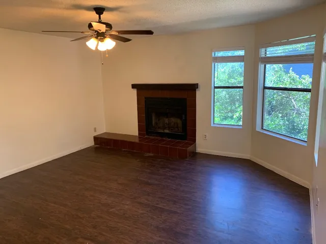 a view of an empty room with wooden floor fireplace and a window