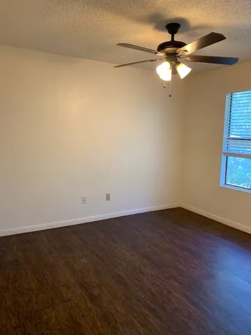 an empty room with wooden floor fan and windows