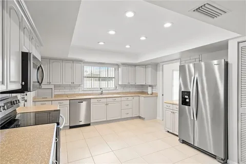 a large white kitchen with a sink and dishwasher a refrigerator with white cabinets