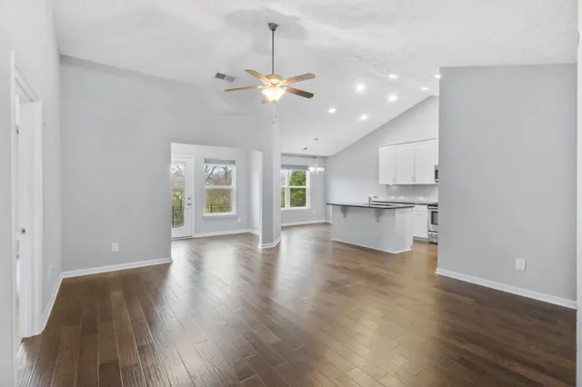 a view of an empty room with wooden floor and a kitchen